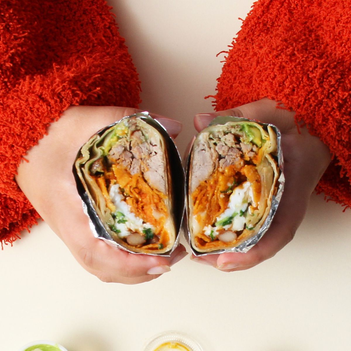 Two hands hold a burrito from Los Burros Supremos.