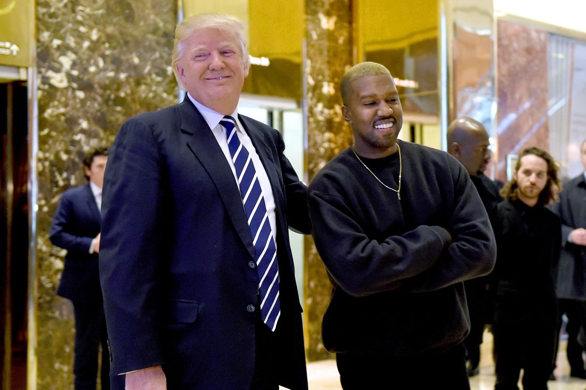 Donald Trump and Kanye West stand next to each other in the lobby of Trump Tower, smiling.