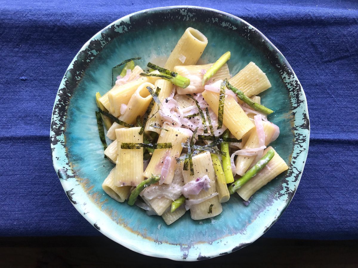 Rigatoni pasta with pink onions, asparagus, and seaweed on a plate.