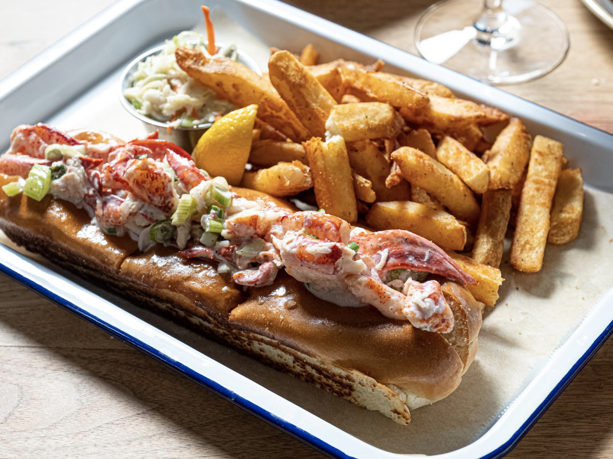 A lobster roll sits on a white plate adjacent french fries