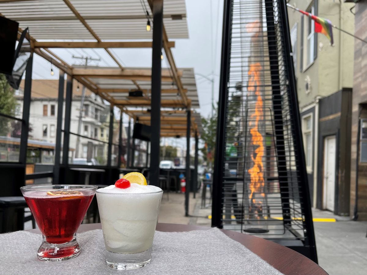 One white slushee cocktail and one dark red cocktail on an outdoor table