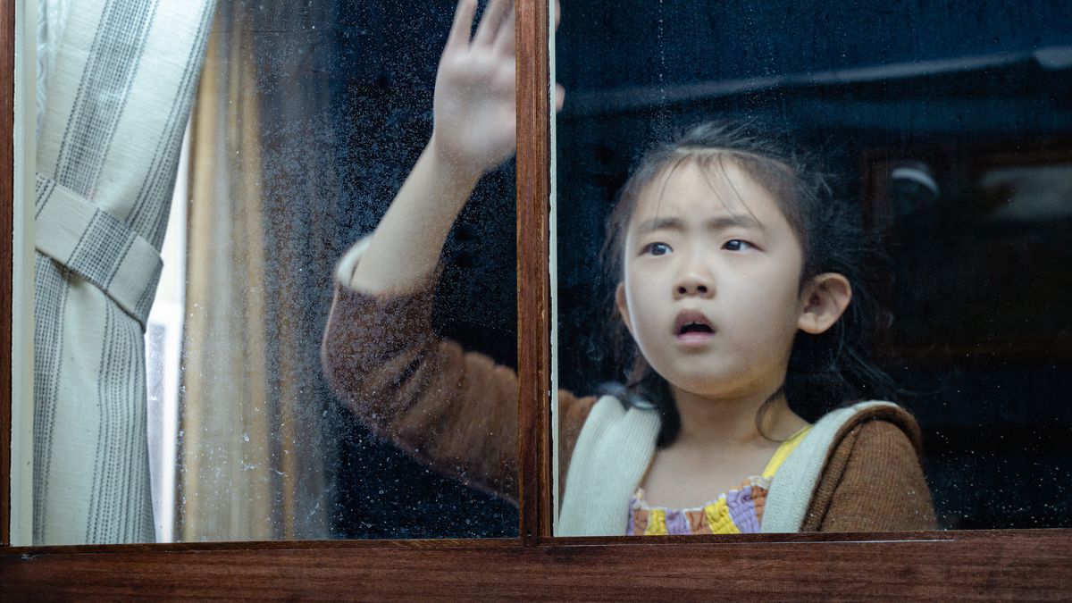 Eight-year-old Wen (Kristen Cui) stands at a window looking out with visible alarm in M. Night Shyamalan’s Knock at the Cabin