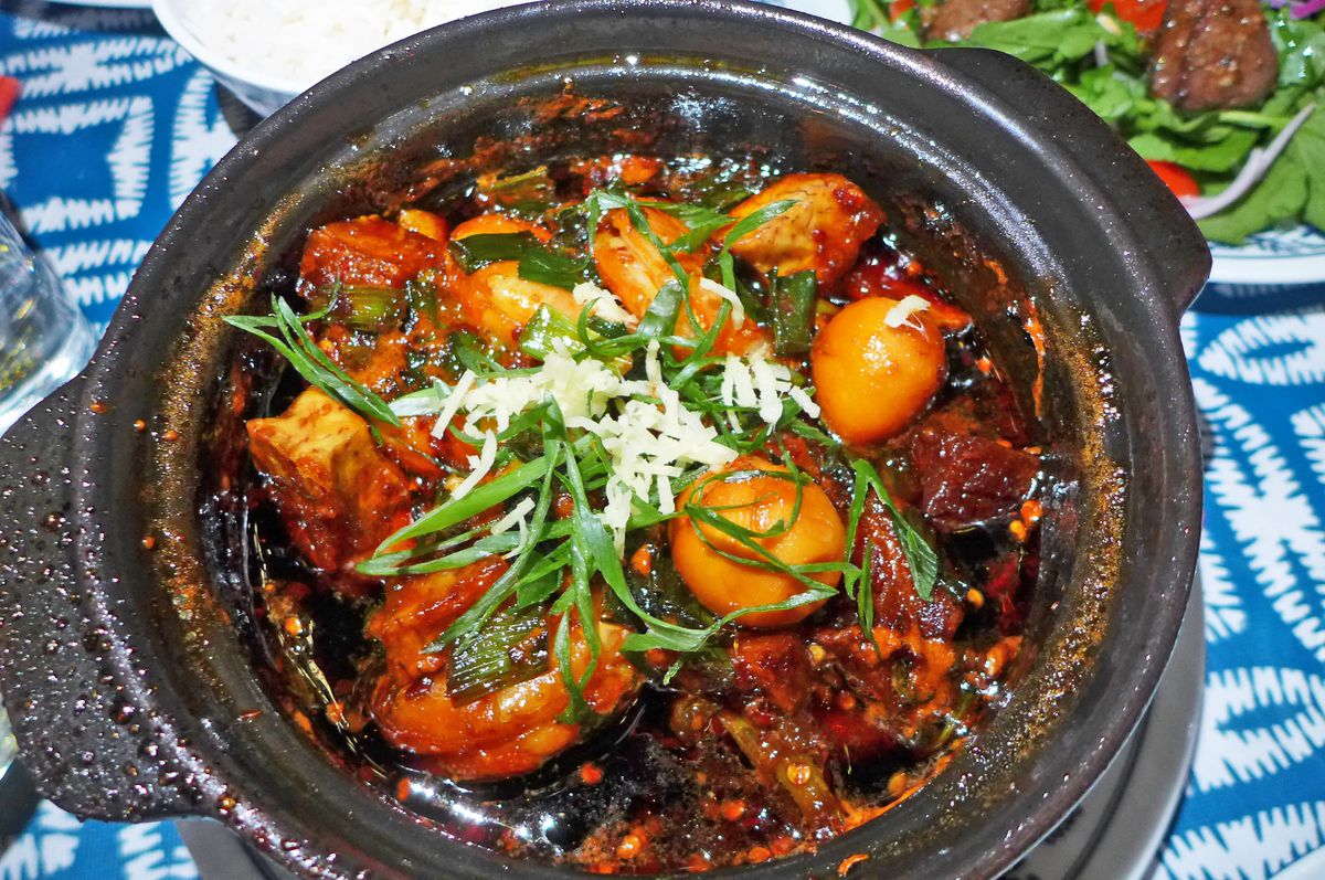 A black metal cauldron with eggs and shrimp in a dark sauce.