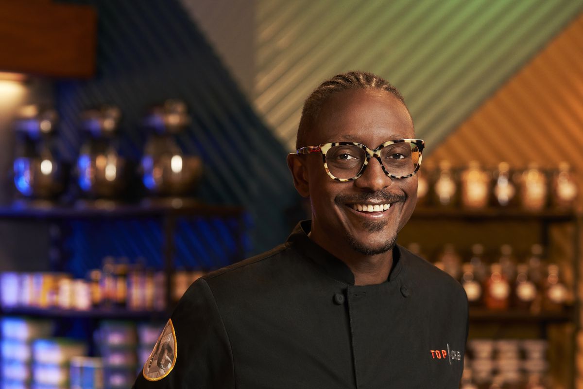 A picture of Gregory Gourdet wearing his black Top Chef uniform in a pantry-style space.
