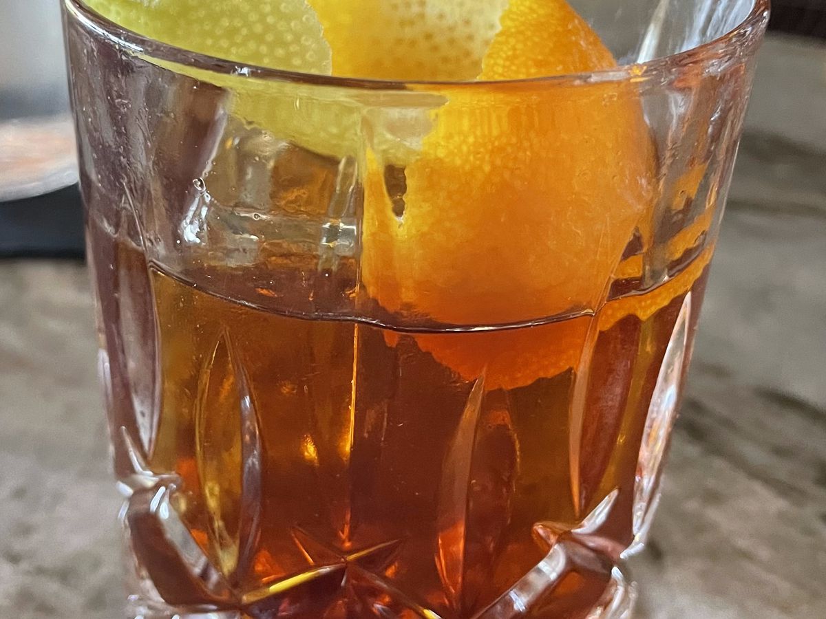 A brown cocktail with an orange peel. 