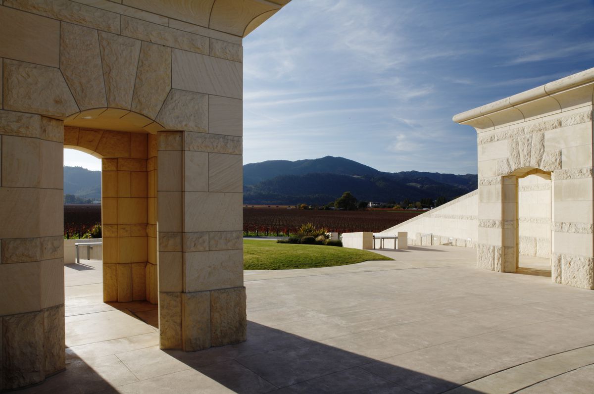 The exterior of Opus One Winery with two limestone building structures in the foreground. In the distance is a mountain landscape.