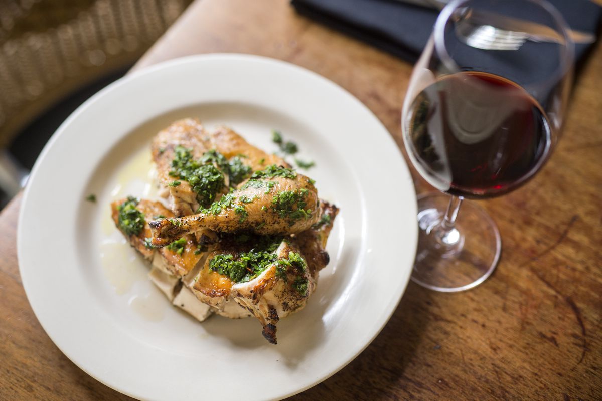 A plate of roast chicken topped with salsa verde beside a glass of wine