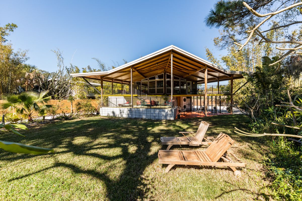 Home with overhanging triangular roof that covers large multi-level patio.