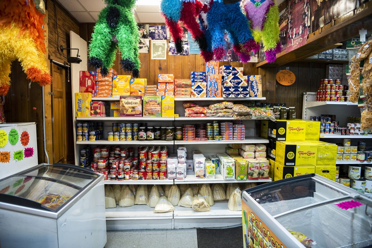 In the foreground, piñatas hanging from the ceiling, freezers to the left and right, a wall shelf filled with packaged food.