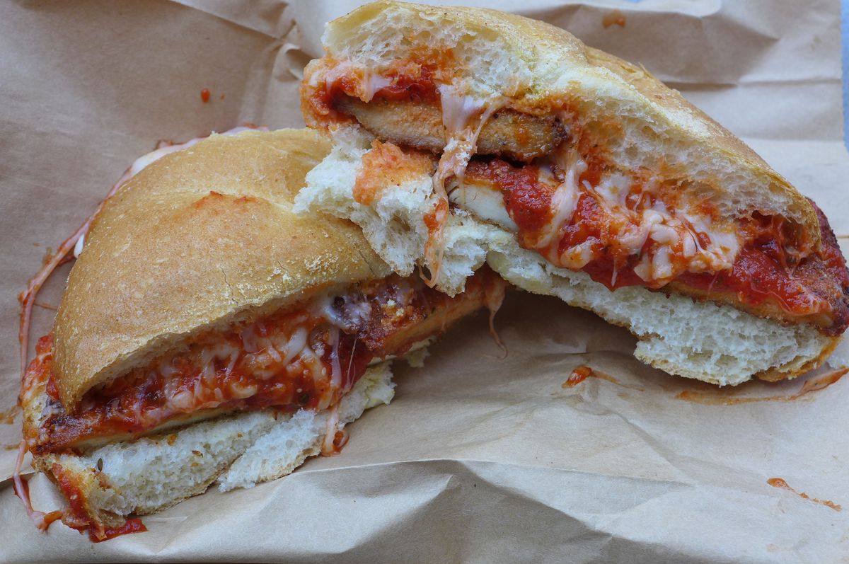 A roll with a crumbed cutlet, cheese, and tomato sauce oozing out of the cut surface.
