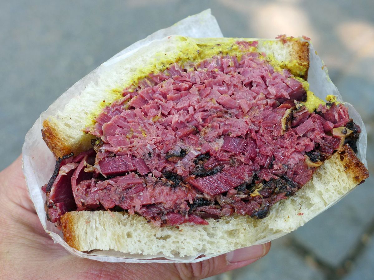 Half of a pastrami sandwich on rye with mustard.