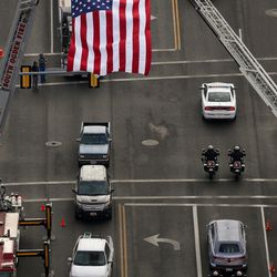 The funeral procession for Utah Highway Patrol trooper Eric Ellsworth passes under an American flag after leaving the Dee Events Center in Ogden on Wednesday, Nov. 30, 2016.