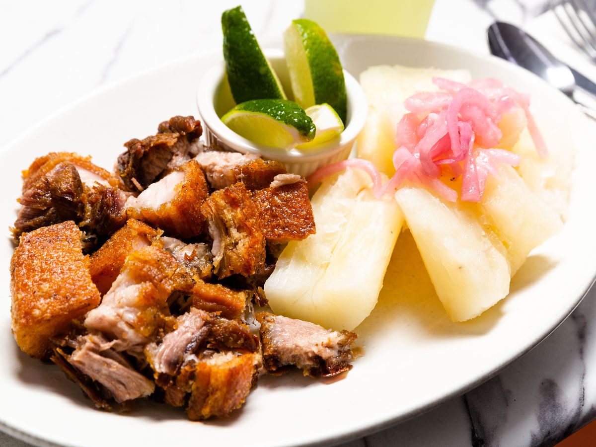 Nuggets of chicharron Dominicano sit next to yucca on a white plate with pickles