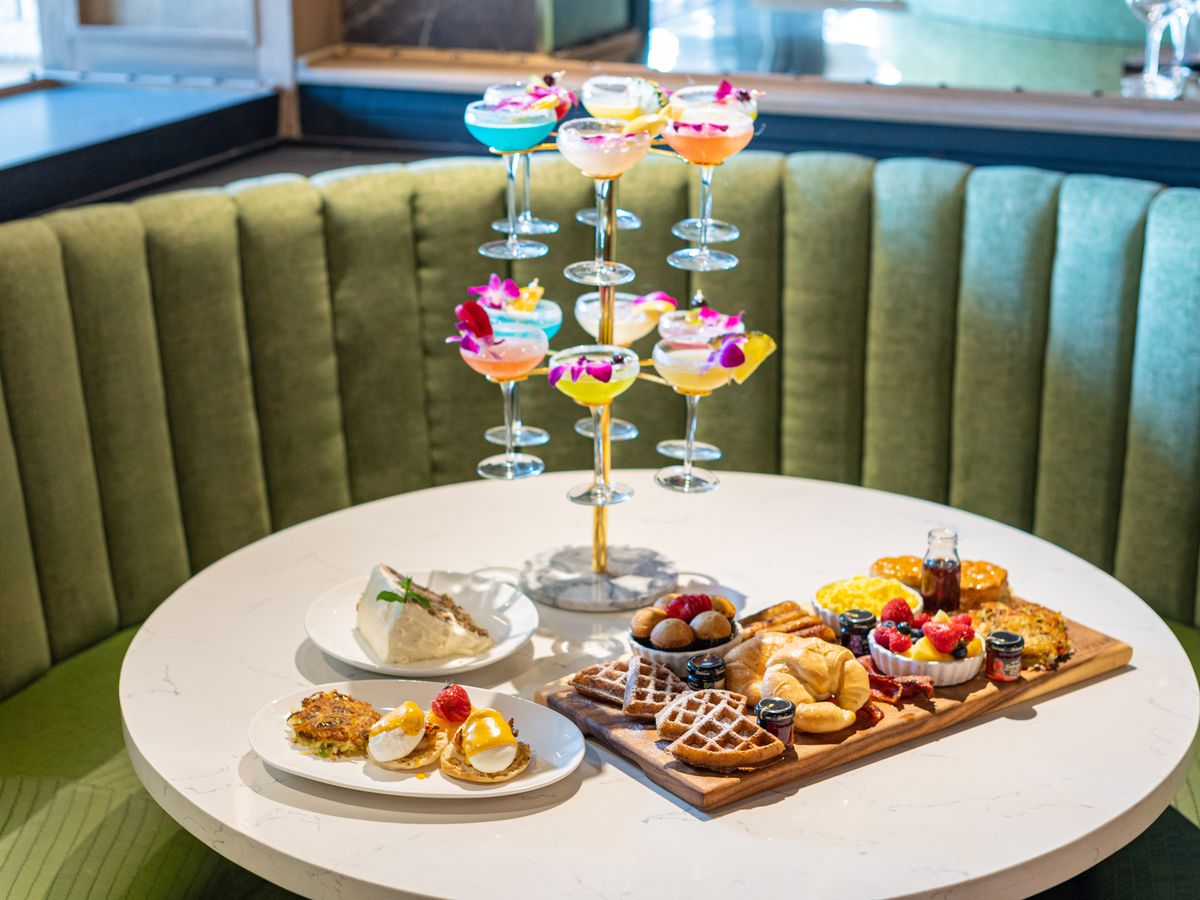 A tower of cocktails with a fruit plate and a breakfast board on a table.