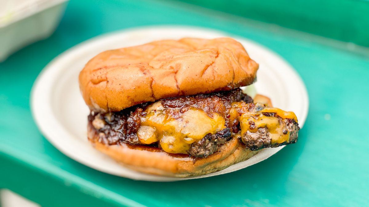 A close up shot of a griddled burger with lots of cheese on a green table.