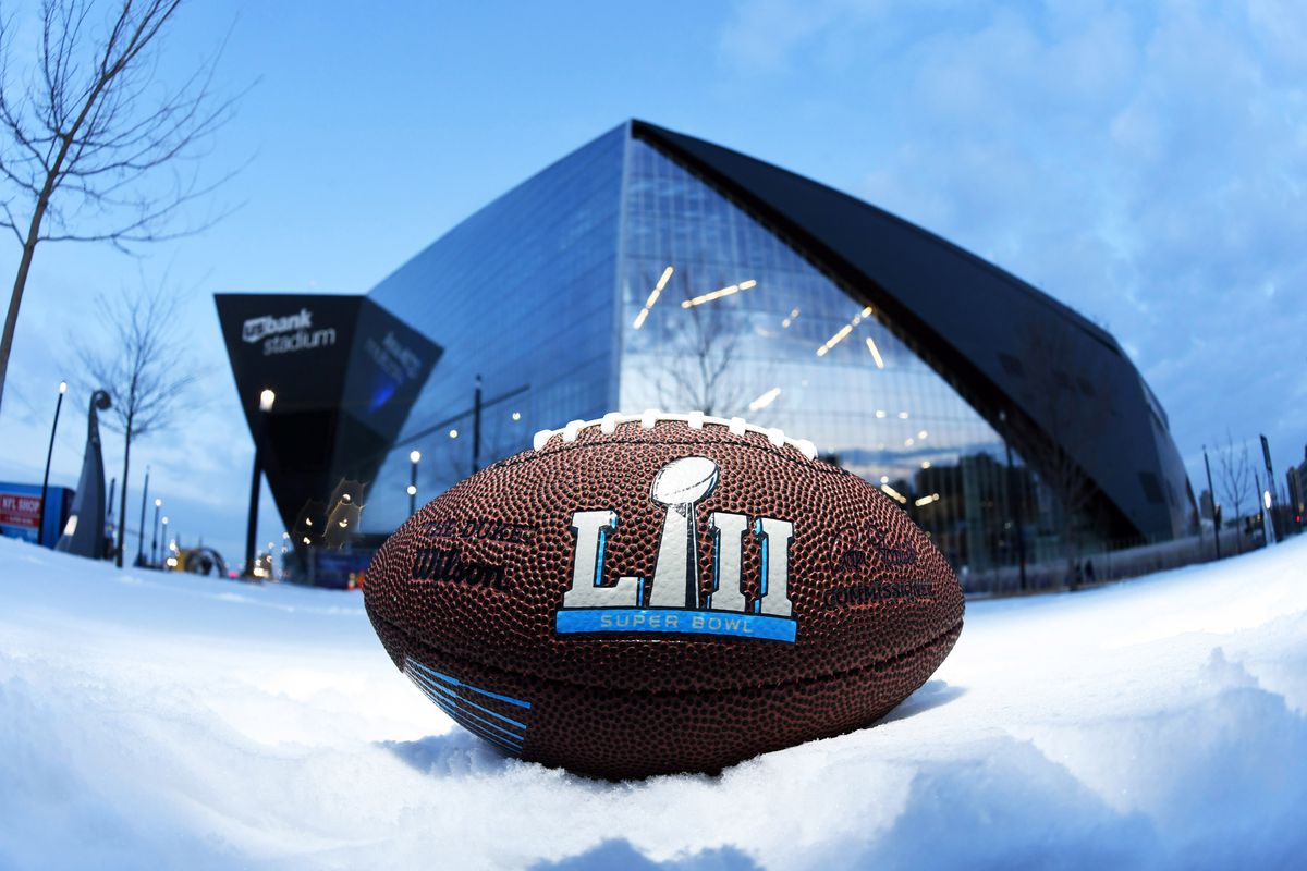 A football that reads “52” in Roman numerals sits on the snowy ground in front of the Super Bowl stadium