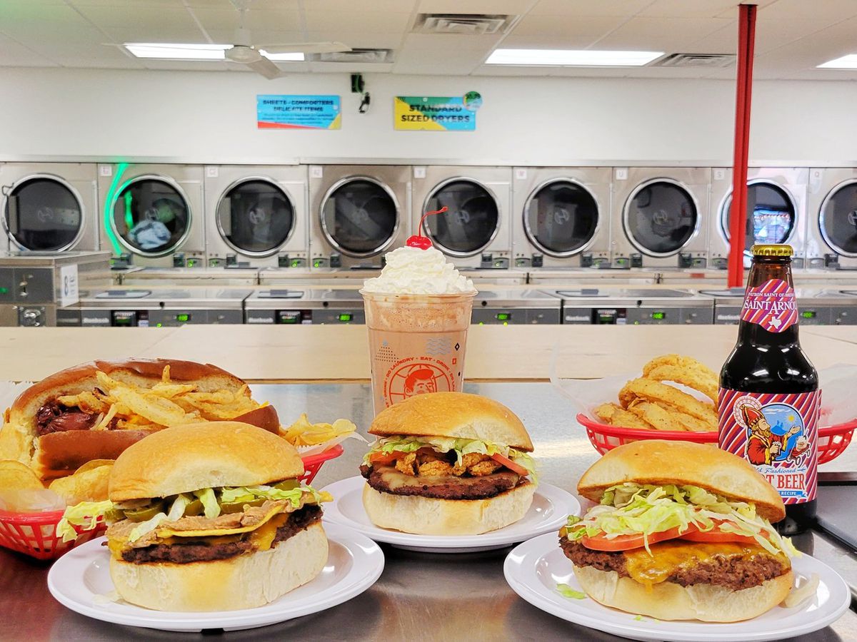 Burgers and beers on a table in front of washing machines.