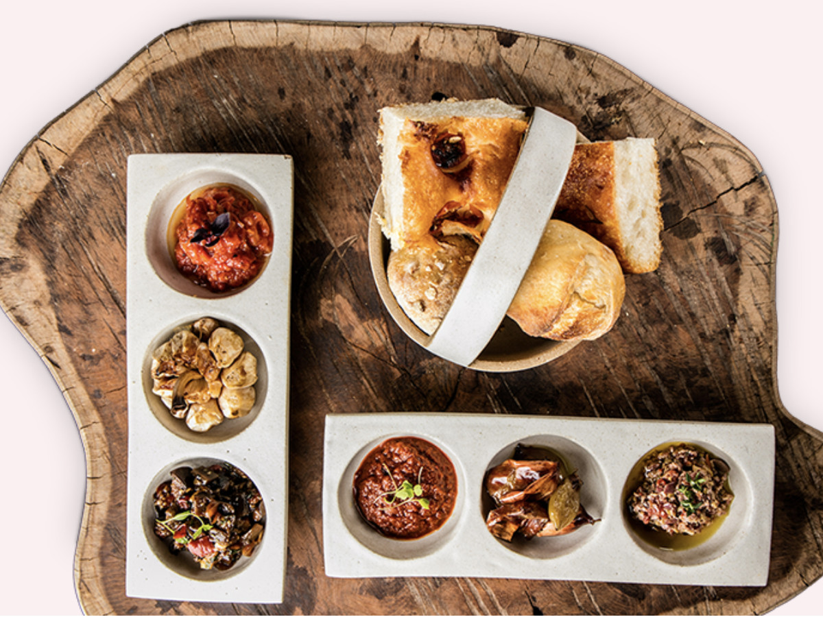 From above, a series of breads with dips and small bites presented on a large wooden serving tray. 