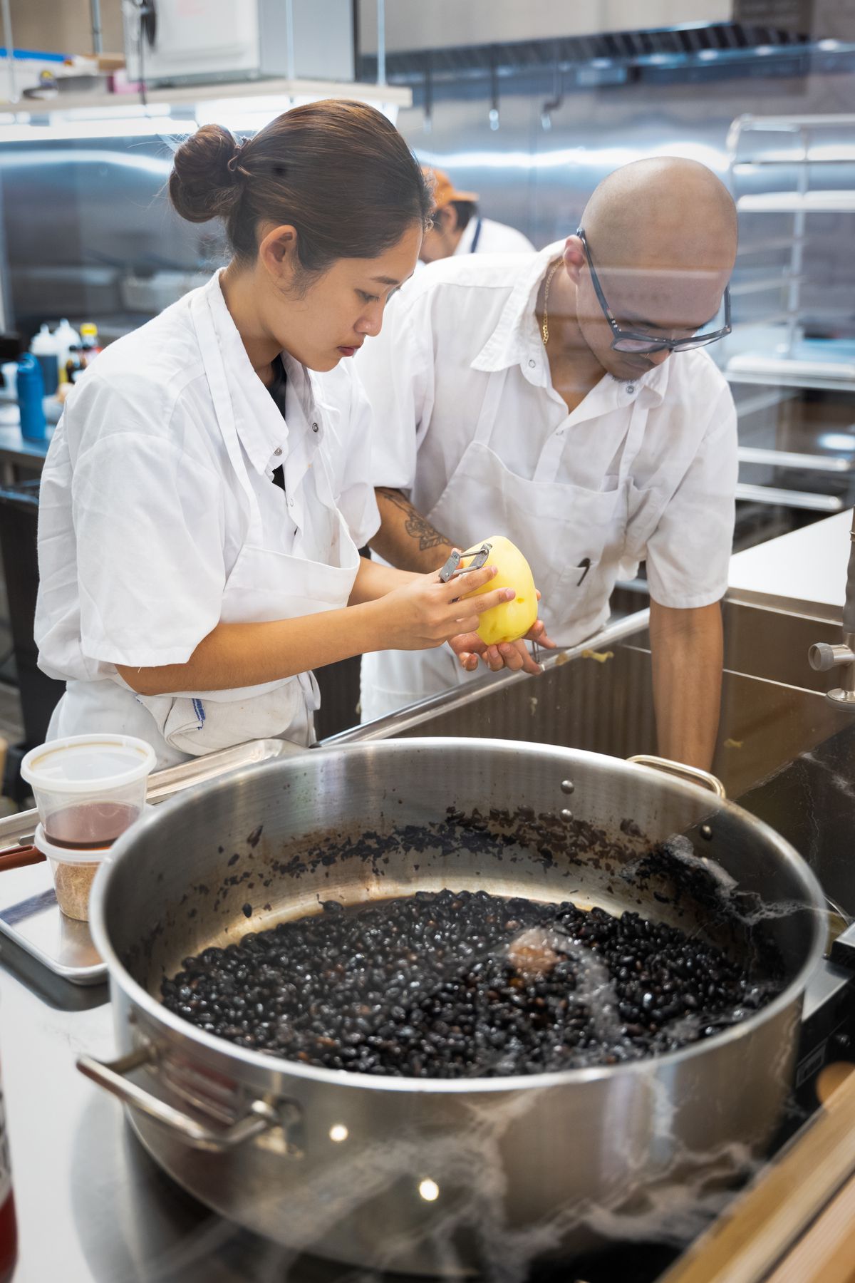 Cooks hover over a pot of black beans.
