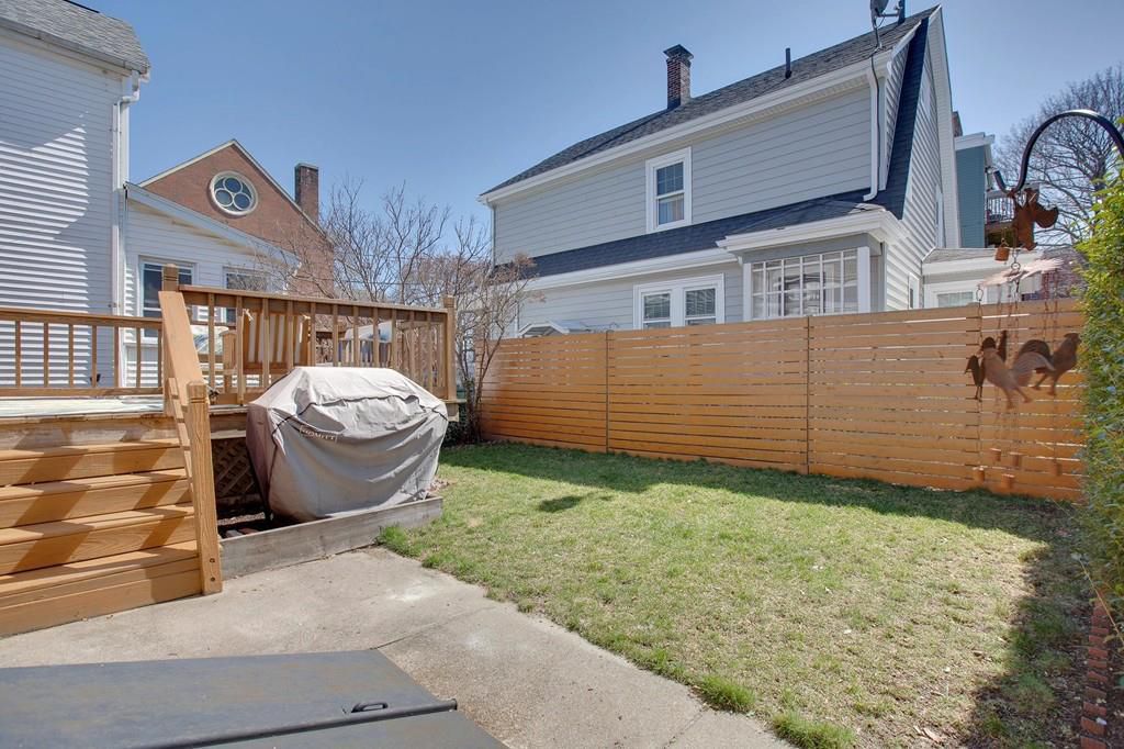 A yard with a deck and a grill with its cover on. 