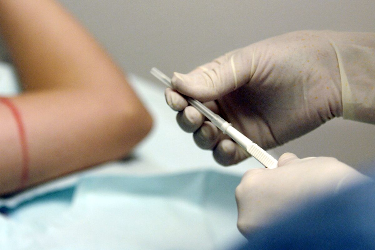 A nurse wearing rubber gloves holds a tube-shaped device to insert a contraceptive implant, while the patient’s arm is seen in the background.