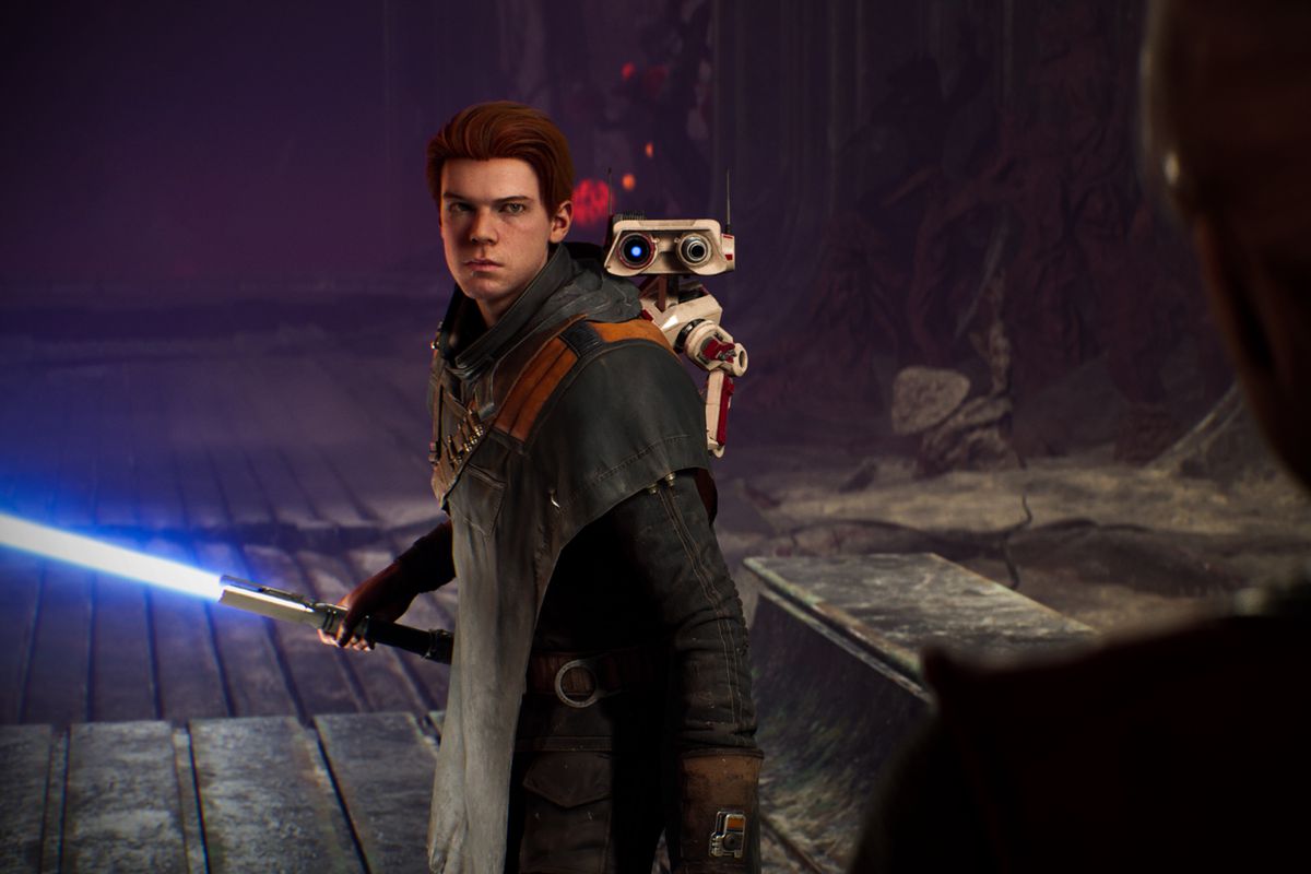 a young brown-haired man, Cal Kestis, holds a blue lightsaber in a screenshot from Star Wars Jedi: Fallen Order