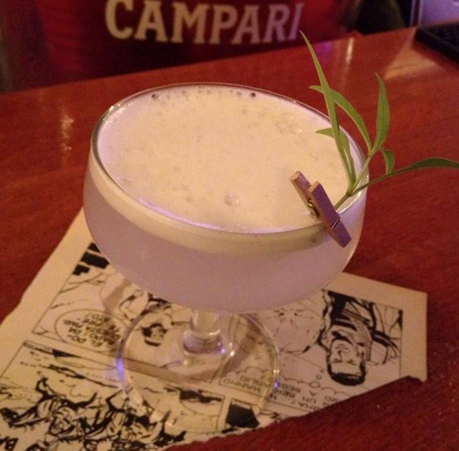 A frothy cocktail, served with a sprig of herbs pinned to the rim with a tiny clothespin 