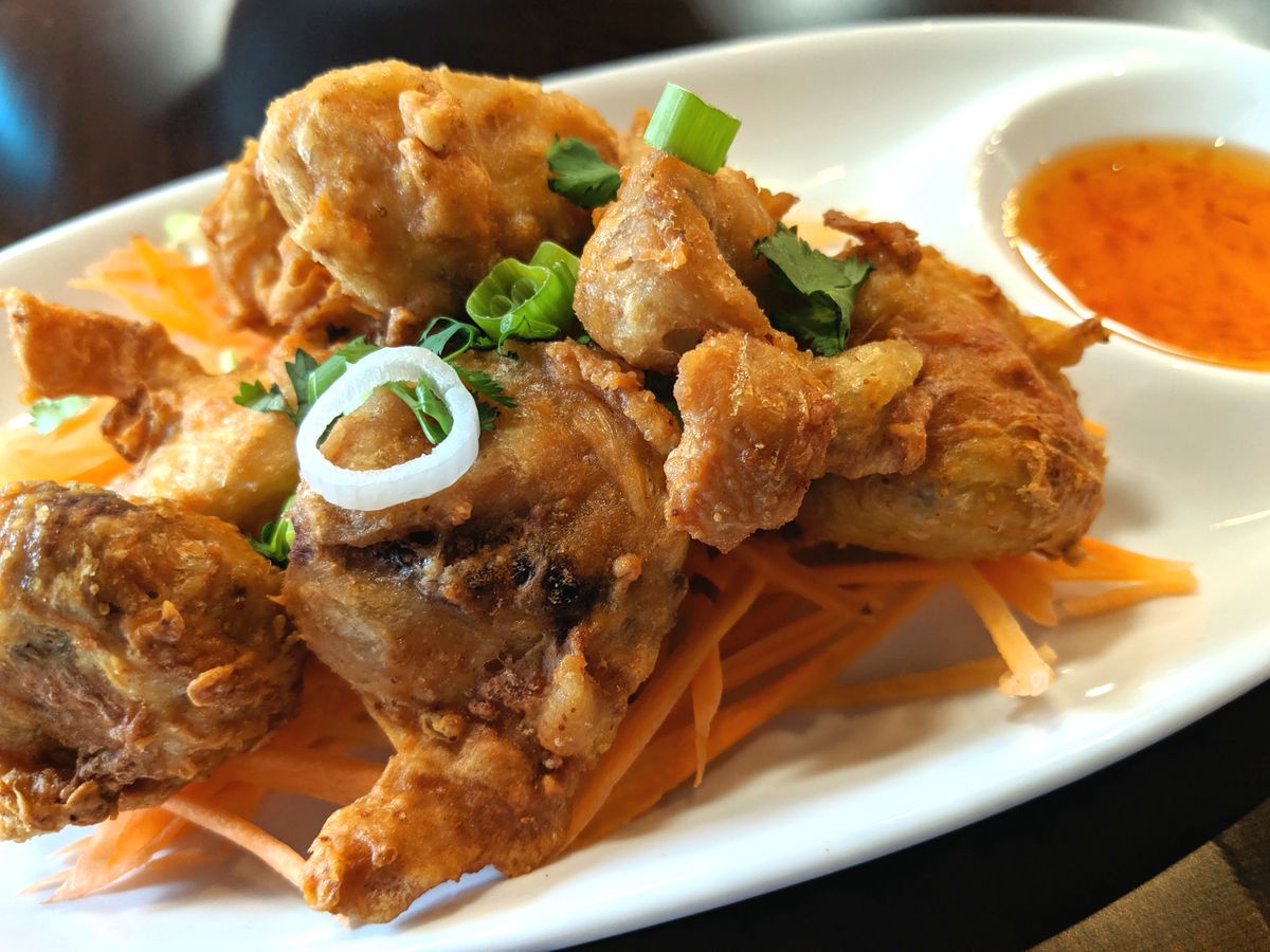 Fried pieces of chicken sit on a bed of carrot strips on a white oval plate with a side bowl of a sweet chile sauce.