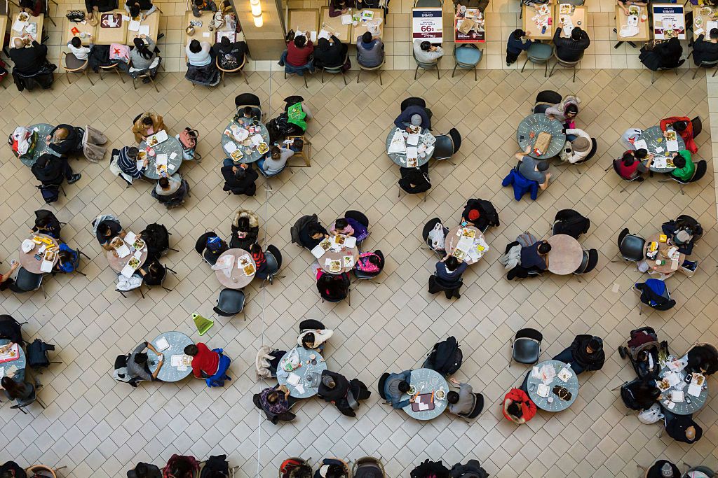 A look down from above on packed tables full of eaters at a mall food court.