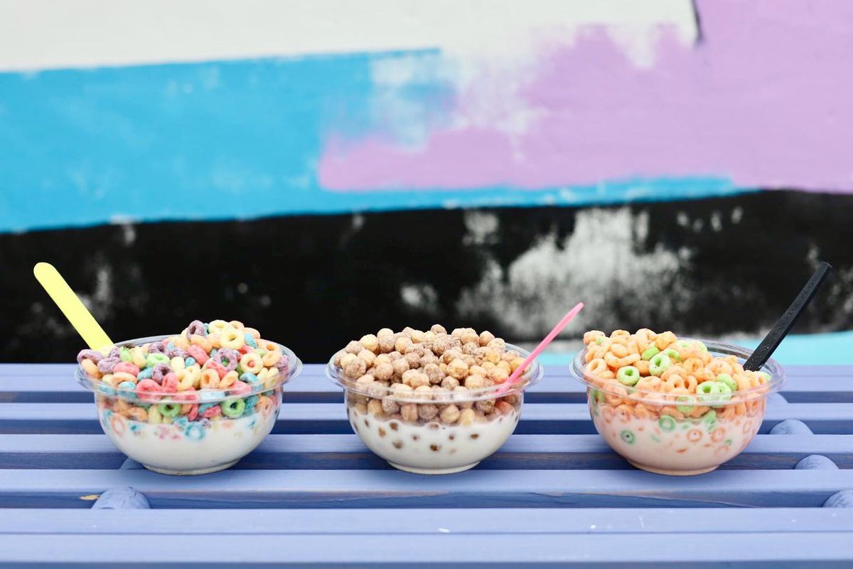 Three bowls of different cereals sitting on a purple wooden bench
