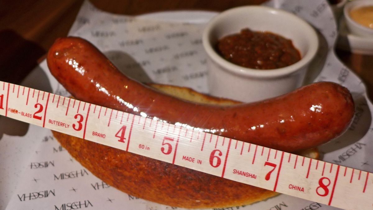 A hot dog in a bun with a tape measure next to it.