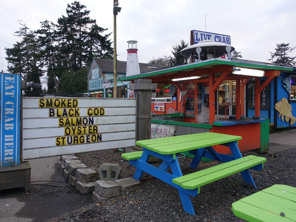 A sign and picnic tables outside a colorful seafood market.