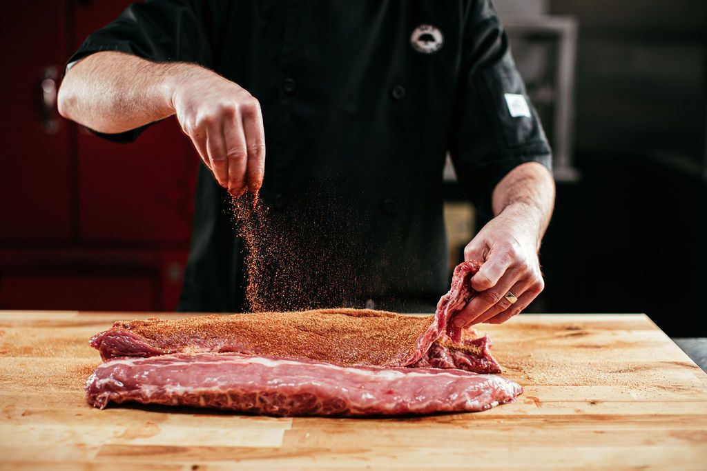 a person sprinkling dry rub on a rack of ribs