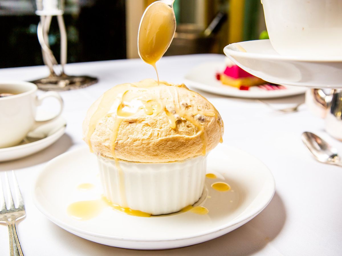 A bread pudding soufflé in a white ramekin on a white plate on a table covered in a white table cloth, with other dishes visible in the background.
