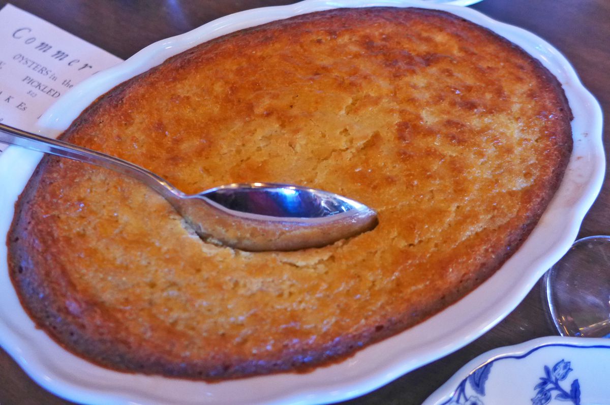 A plate of a sort of bread pudding, smooth with a spoon stuck in the middle.