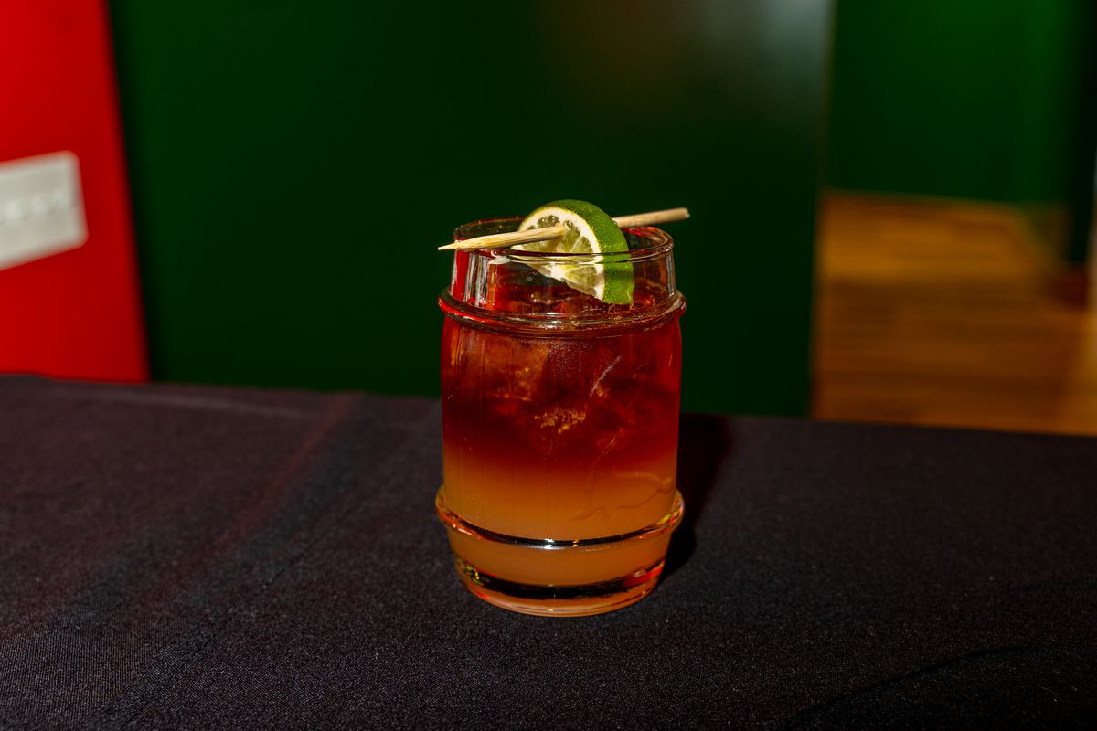 A layered red and orange cocktail with a slice of lime garnish.