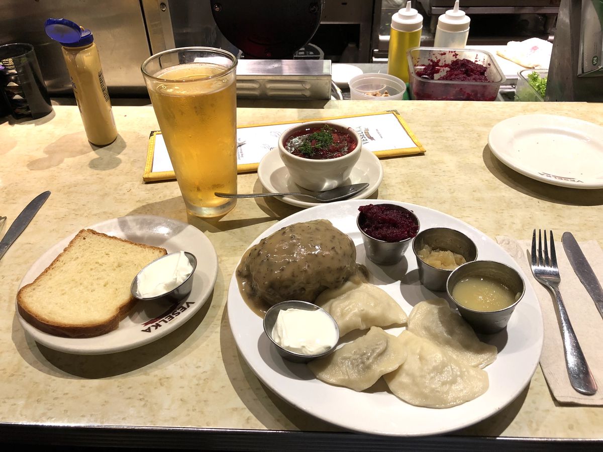 A photograph of a spread filled out with pierogi, a slice of white bread, and a side cup of borscht