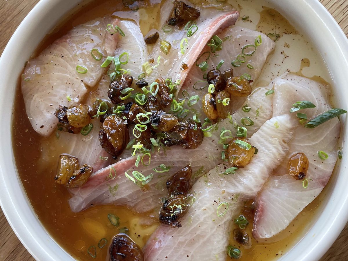 An overhead shot of raw white fish in a thin, yellow broth, topped with sliced chives.