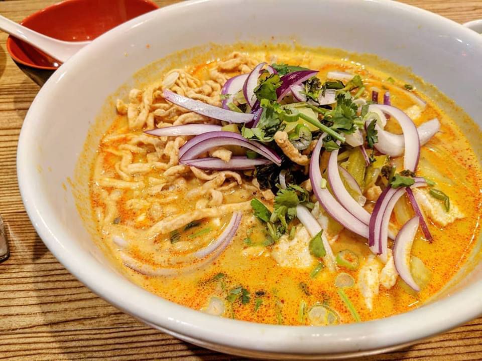 A yellow curry soup with noodles, fried noodles, red onions, cilantro, and more