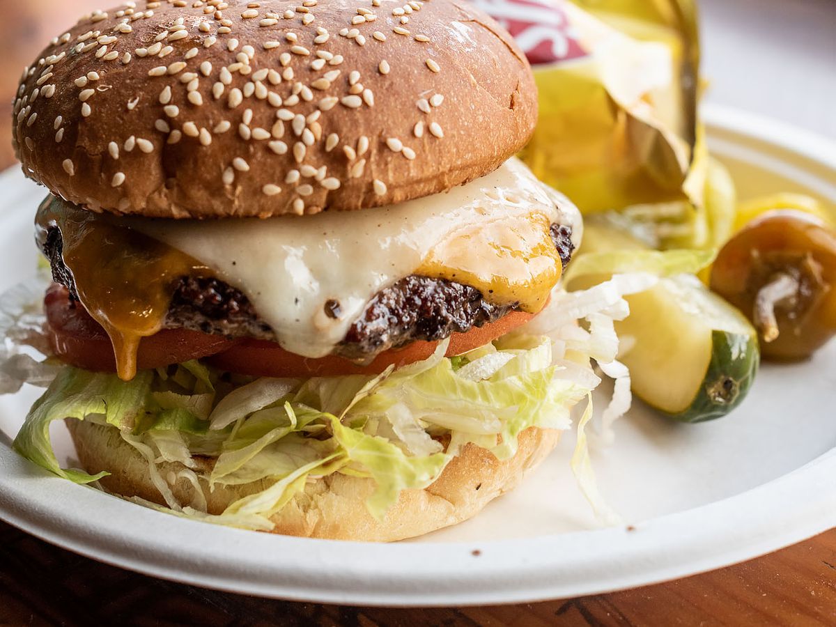 A vertical photo of a cheeseburger with two kinds of cheese on a seeded bun.