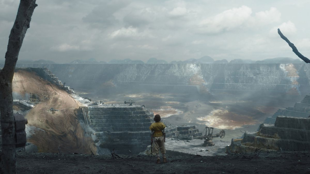 A young kid standing in front of a massive hole in the ground