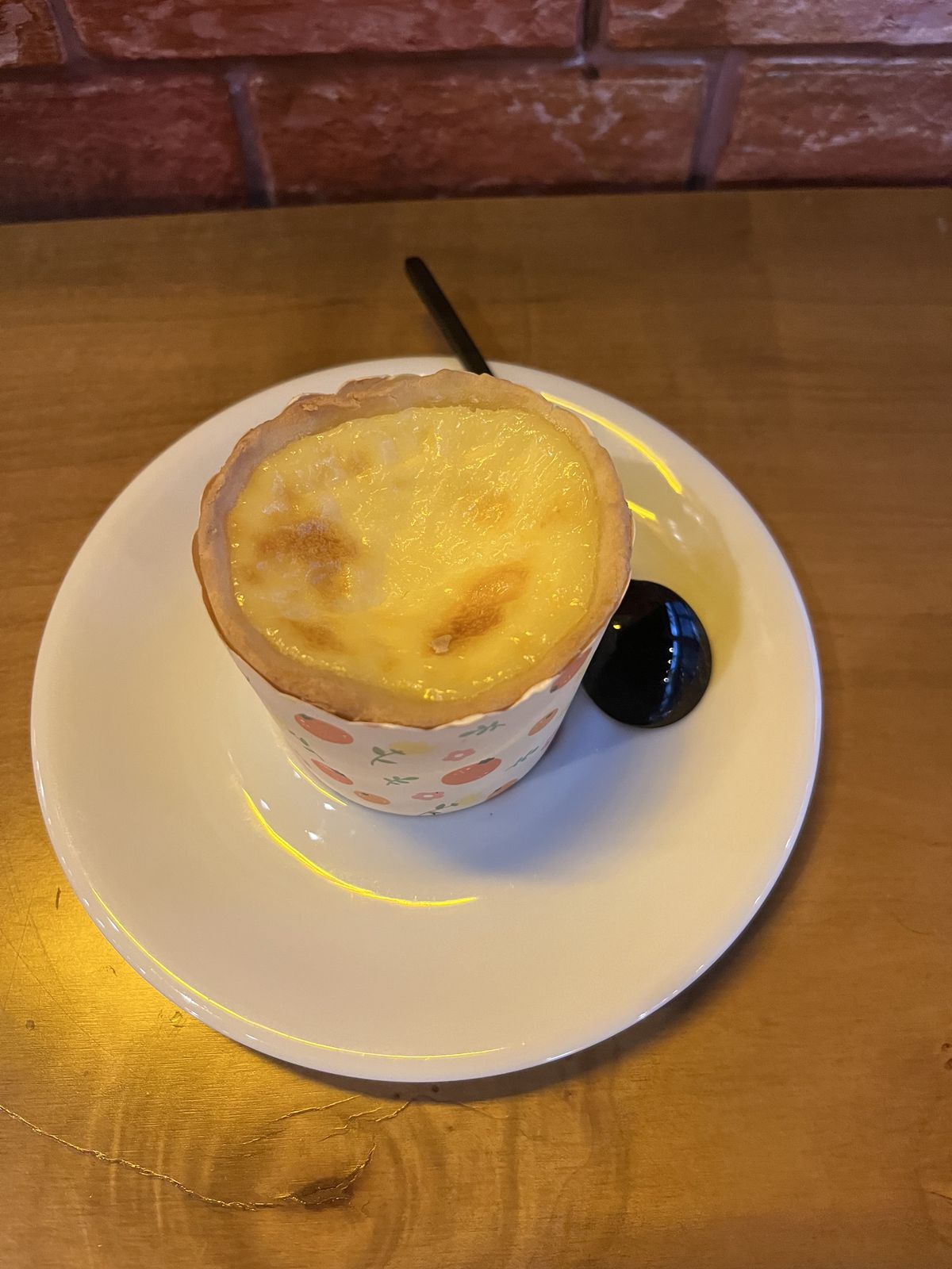 An egg tart on a plate next to a spoon.