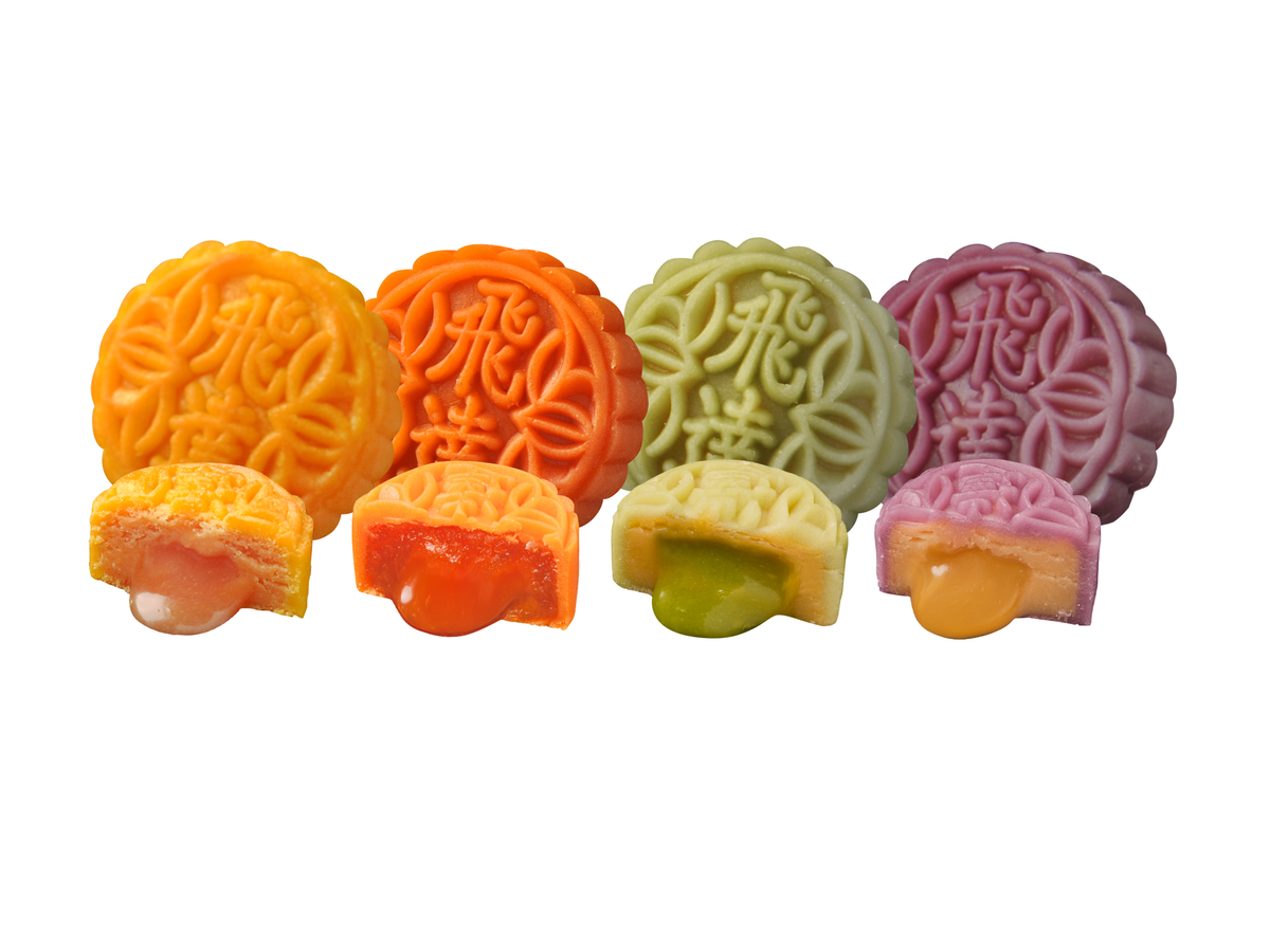 Four colorful mooncakes have fillings oozing out: yellow custard, orange, green matcha, and yellow durian.