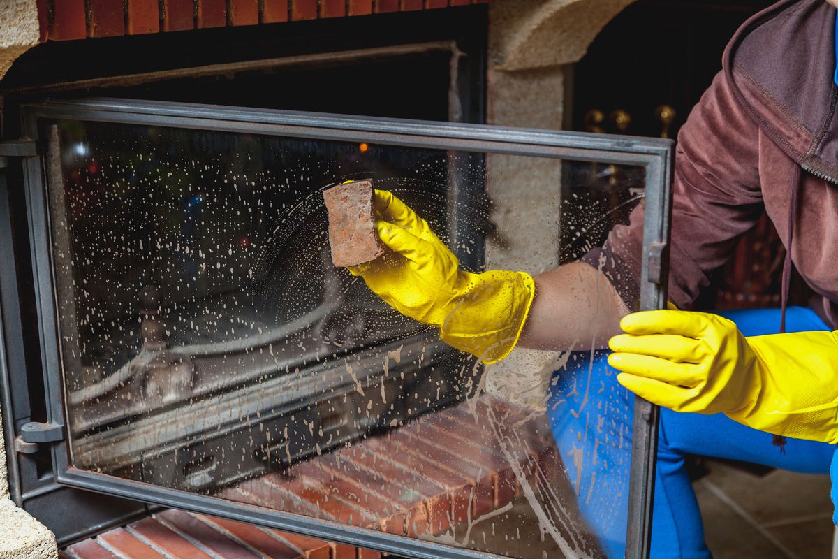 A person cleaning the glass cover of a fireplace.