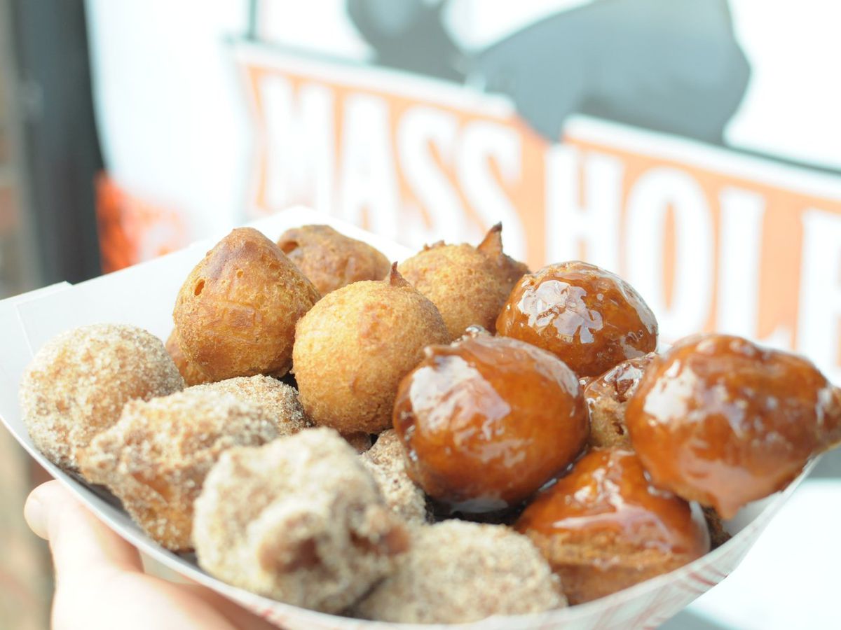 A paper tray brimming with three kinds of doughnut holes topped with cinnamon sugar, caramel sauce, and plain