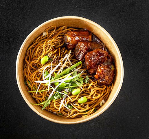 A bowl of noodles with edamame and ribs on a black background