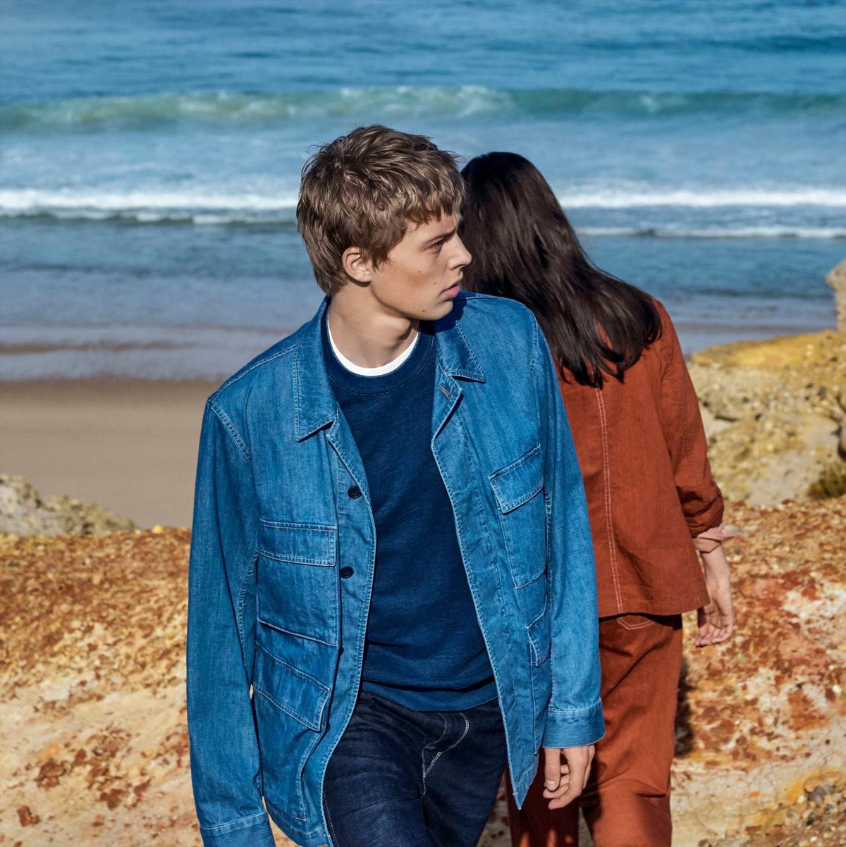 A male model in a denim jacket in the Uniqlo U lookbook, posing with a female model in a rust jacket