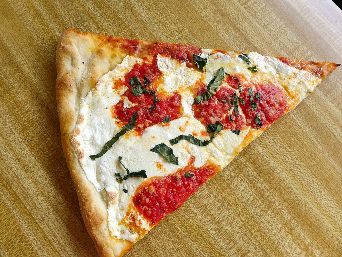 A wedge shaped slice with plenty of white cheese and shredded basil.