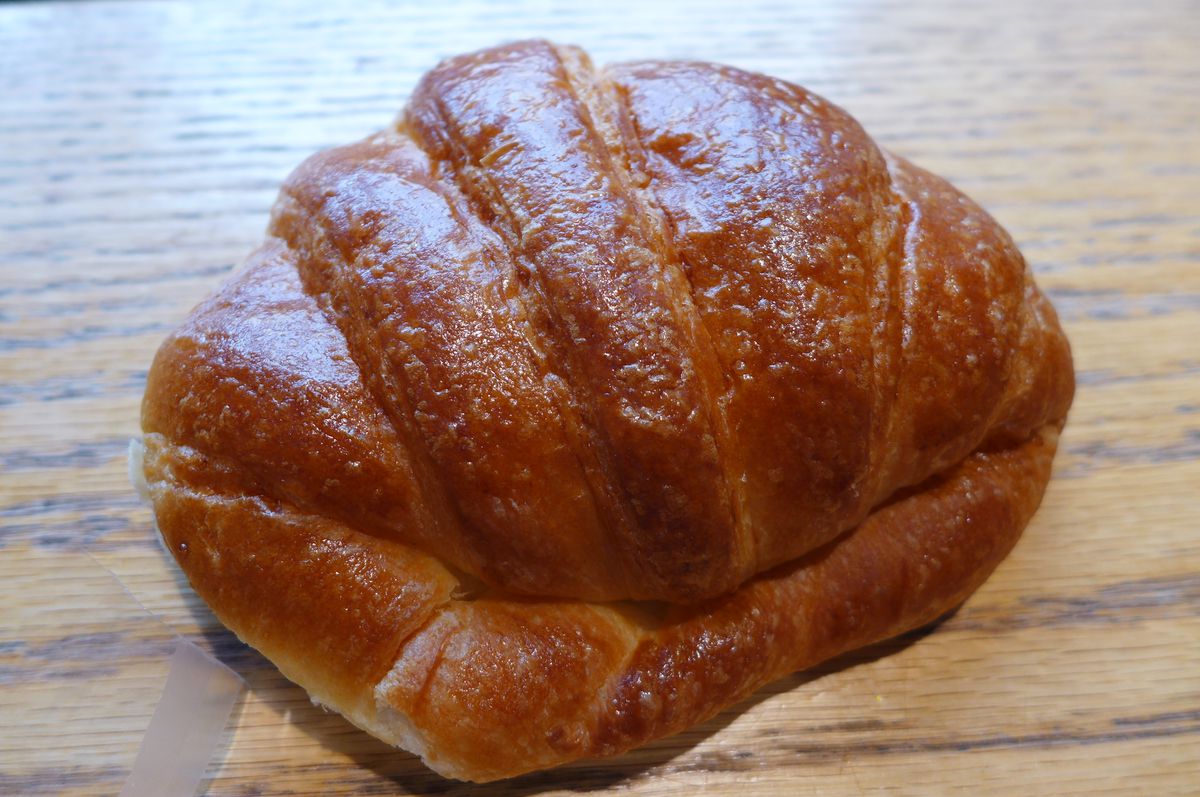 A roundish compact croissant on a grained wooden background.