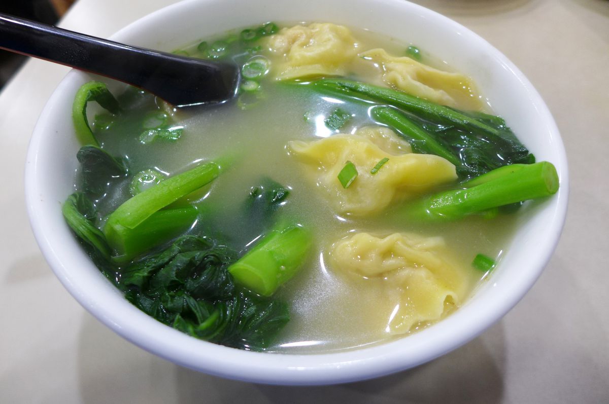 A white bowl with a soup in it from within which yellow dumplings are seen peeking out along with leafy greens.